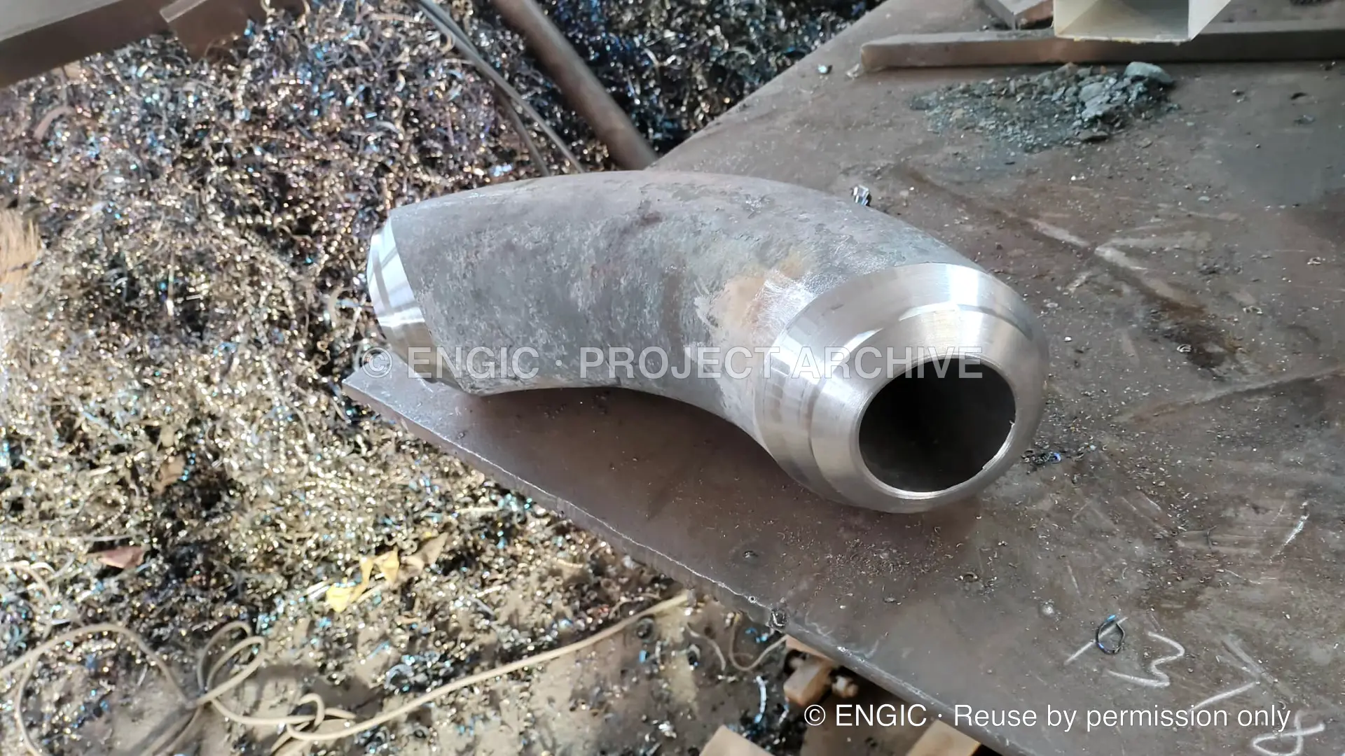 A heavy-wall pipe elbow with freshly machined ends on a workshop bench
