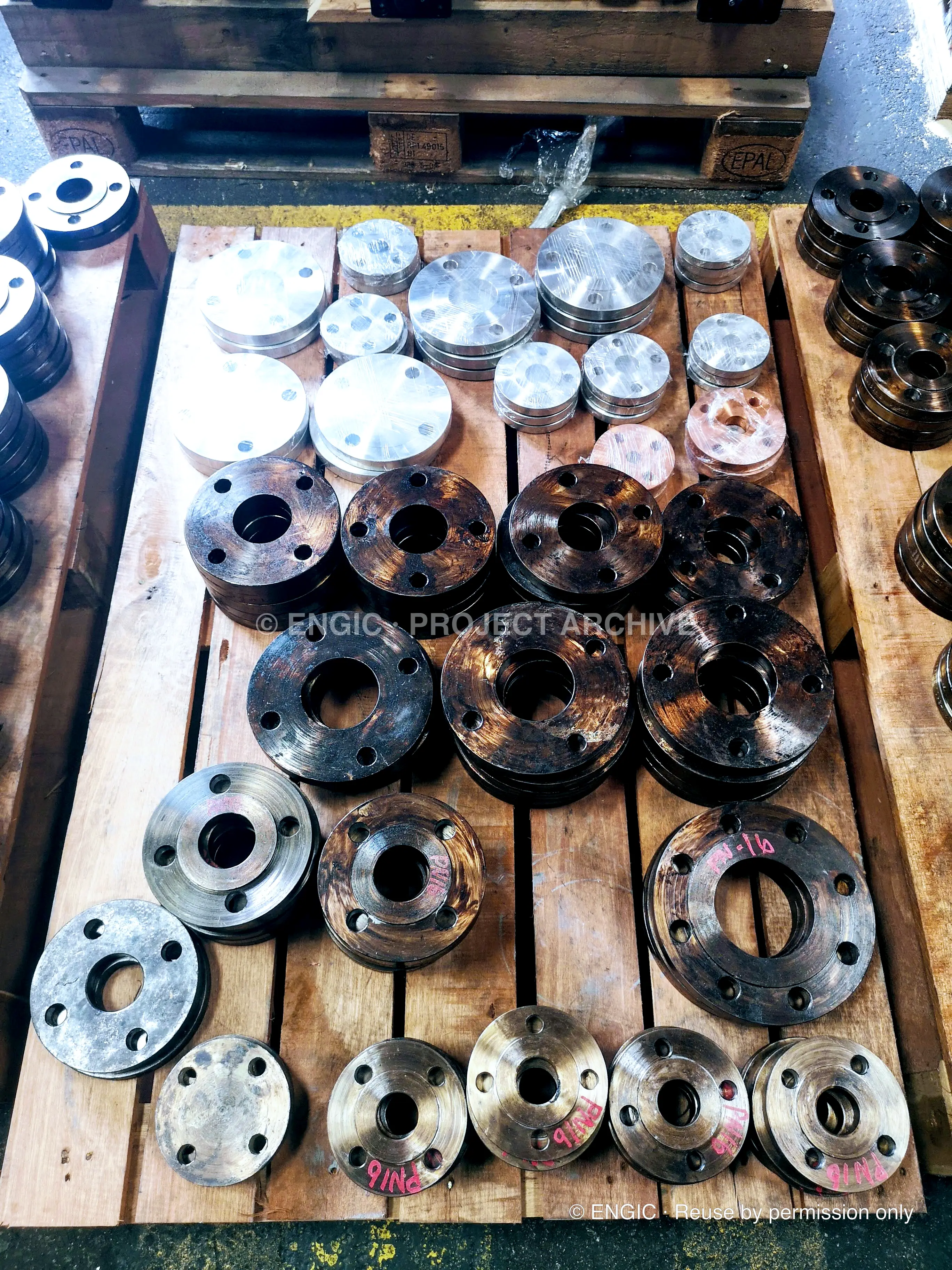 Assorted flanges in bright and darkened finishes arranged on a timber pallet