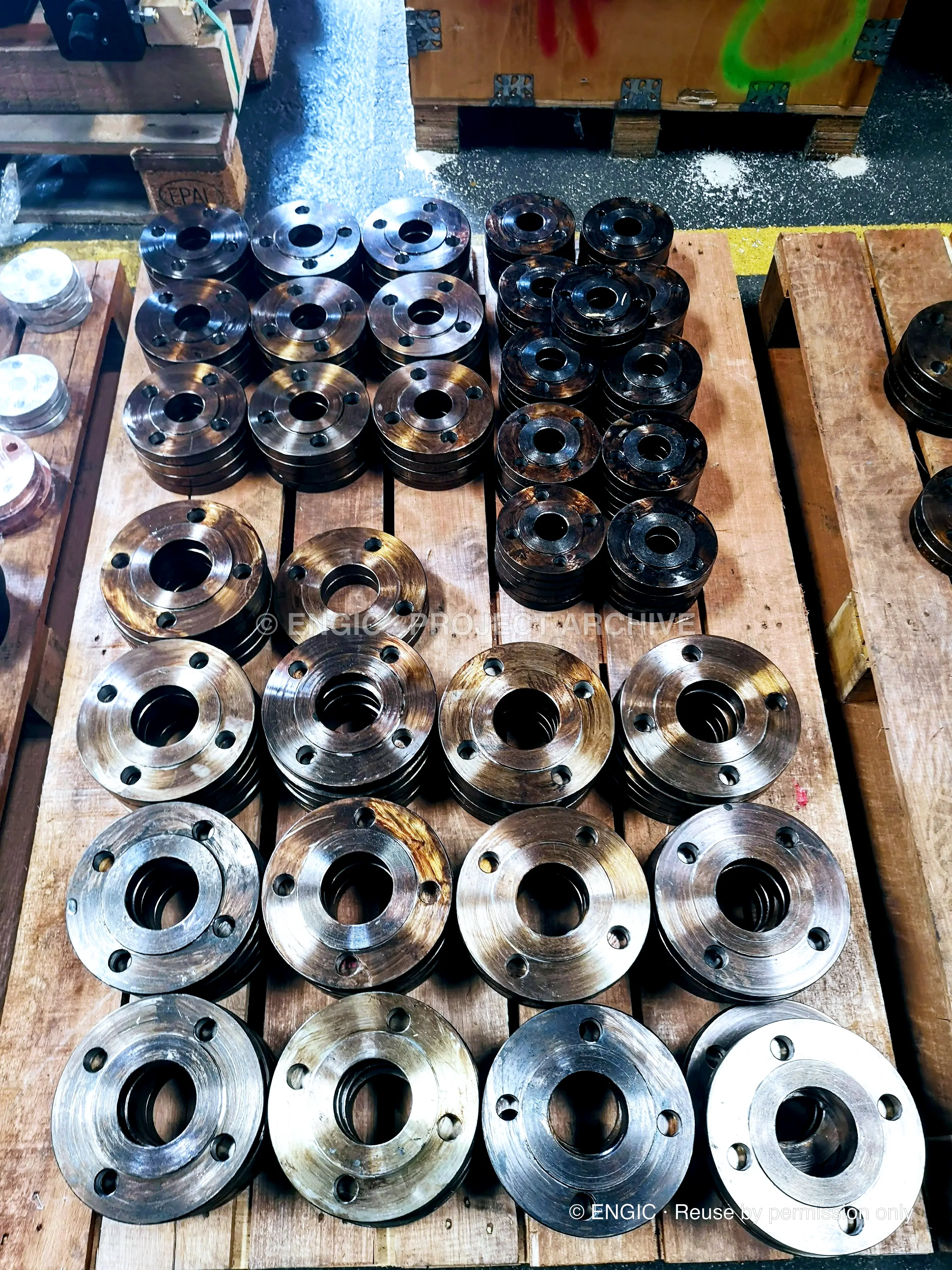 Pallets of flanges in many diameters photographed from above, bronze, black and bright finishes together