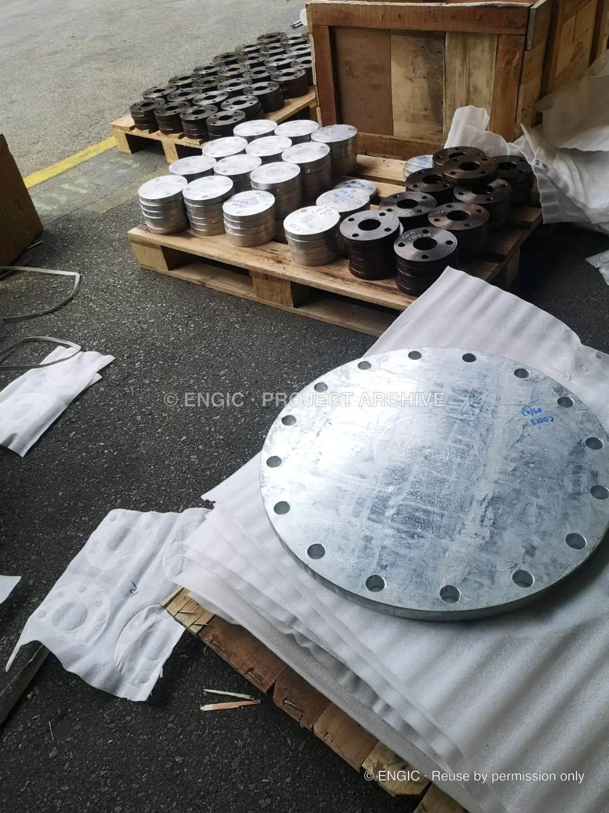 A large drilled blind flange laid out beside other components