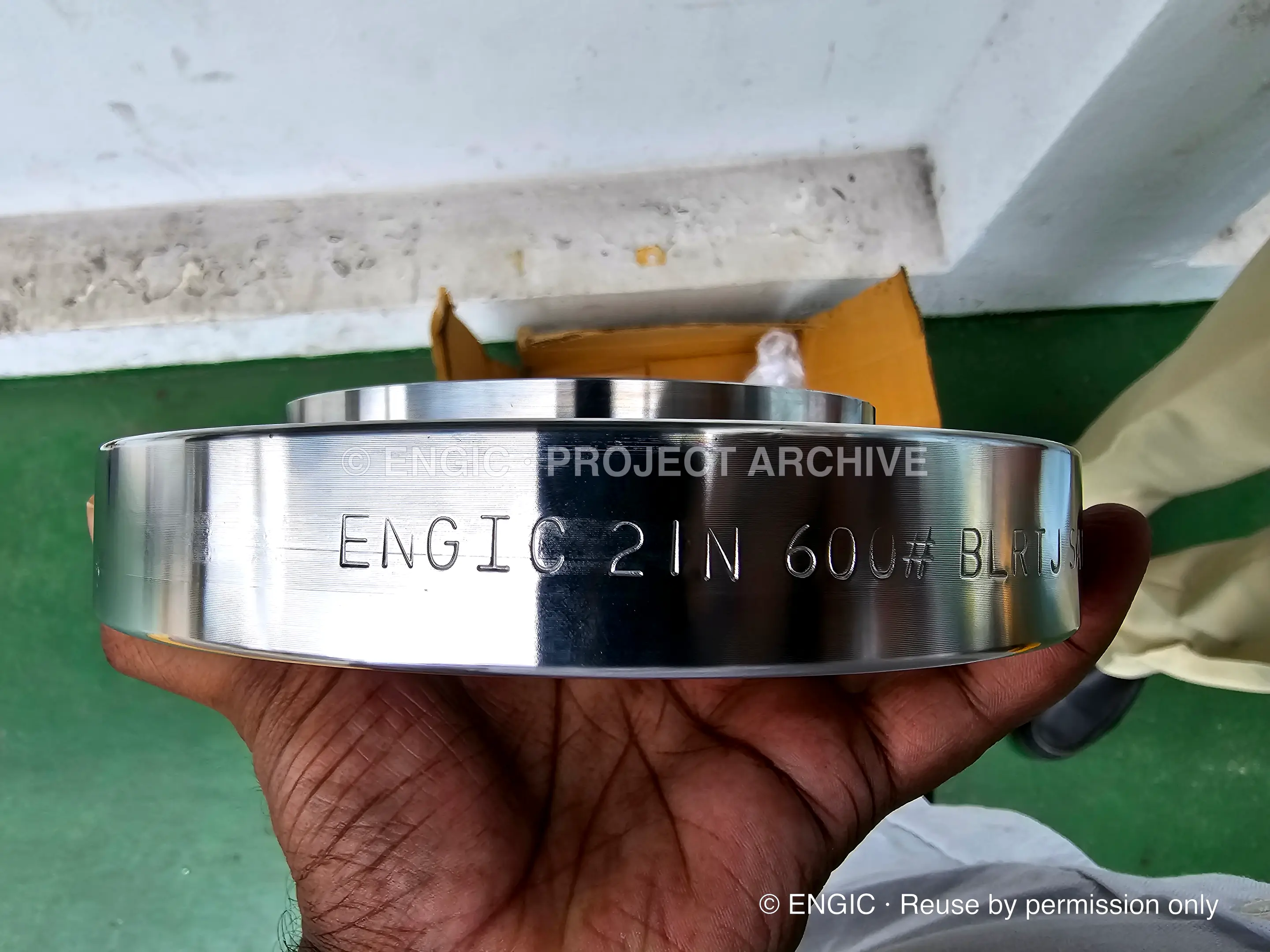 A mirror-polished flange held in one hand, hard-stamped with its Engic designation, size and pressure class