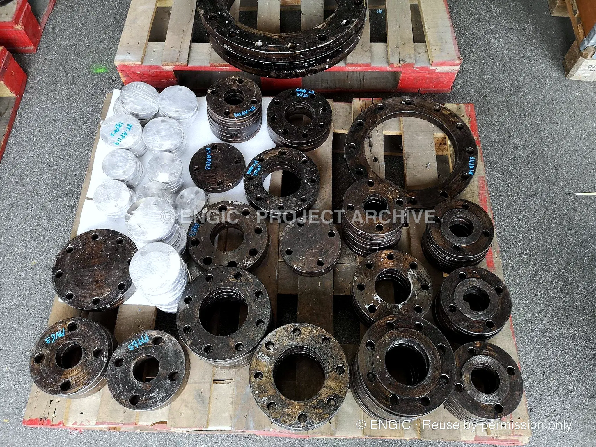Flanges of several sizes and a stack of white gaskets set out across two pallets in a yard