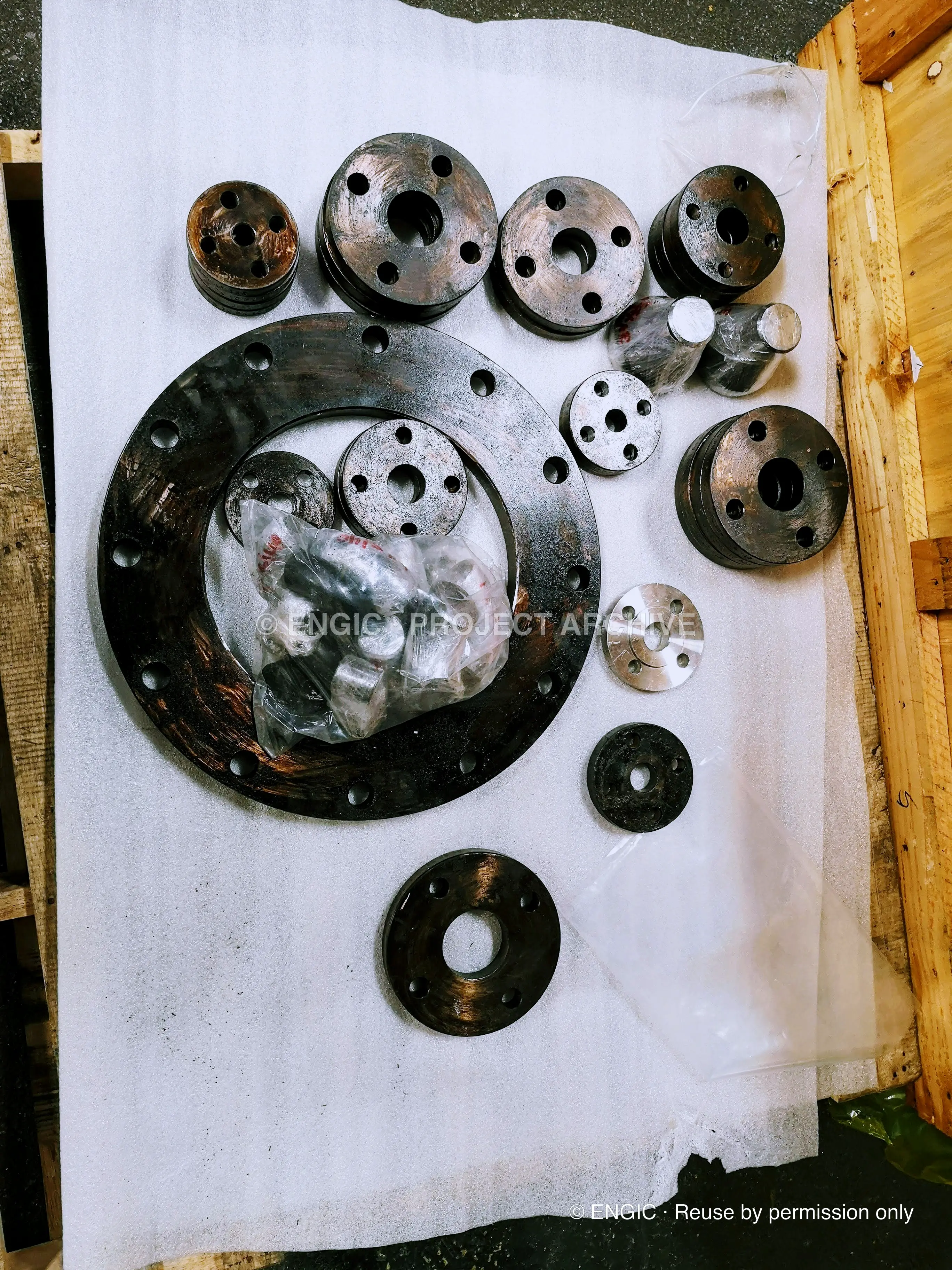 Flanges and gaskets of graduated sizes laid out on white sheeting inside a timber crate