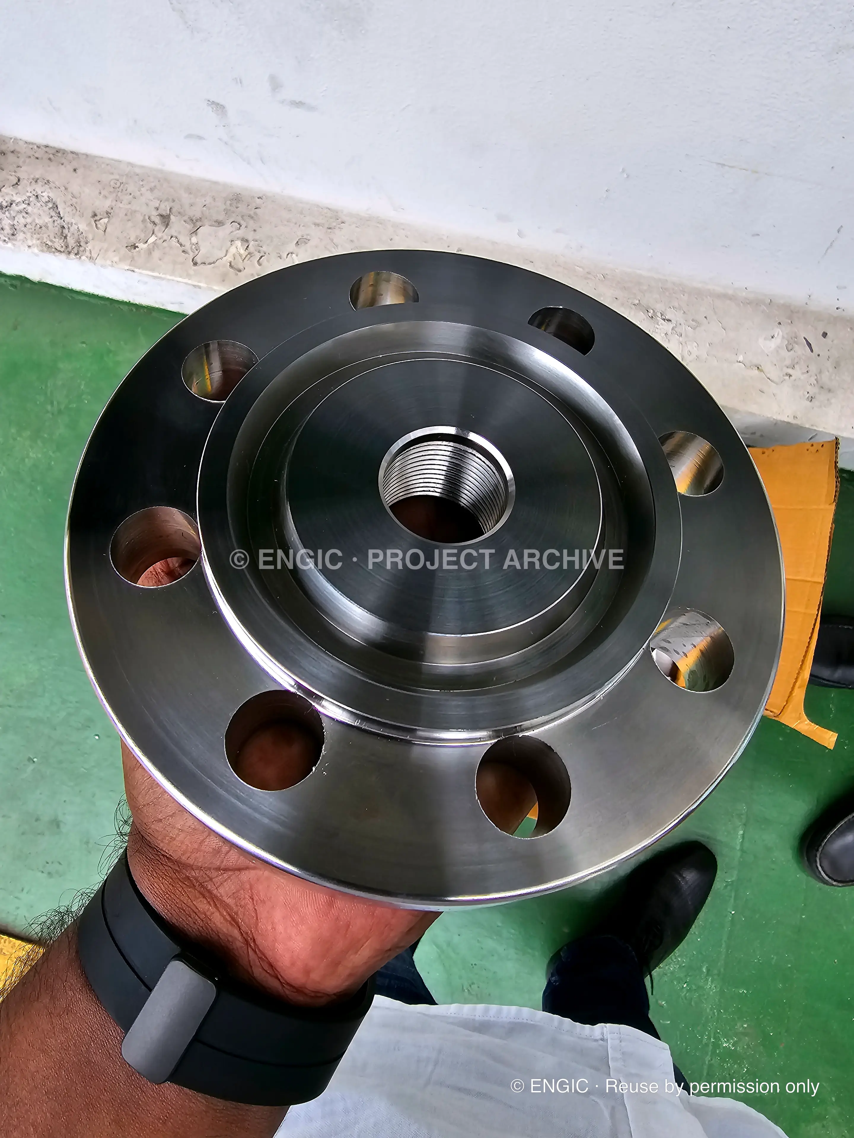 A machined stainless flange with a threaded bore and drilled bolt holes