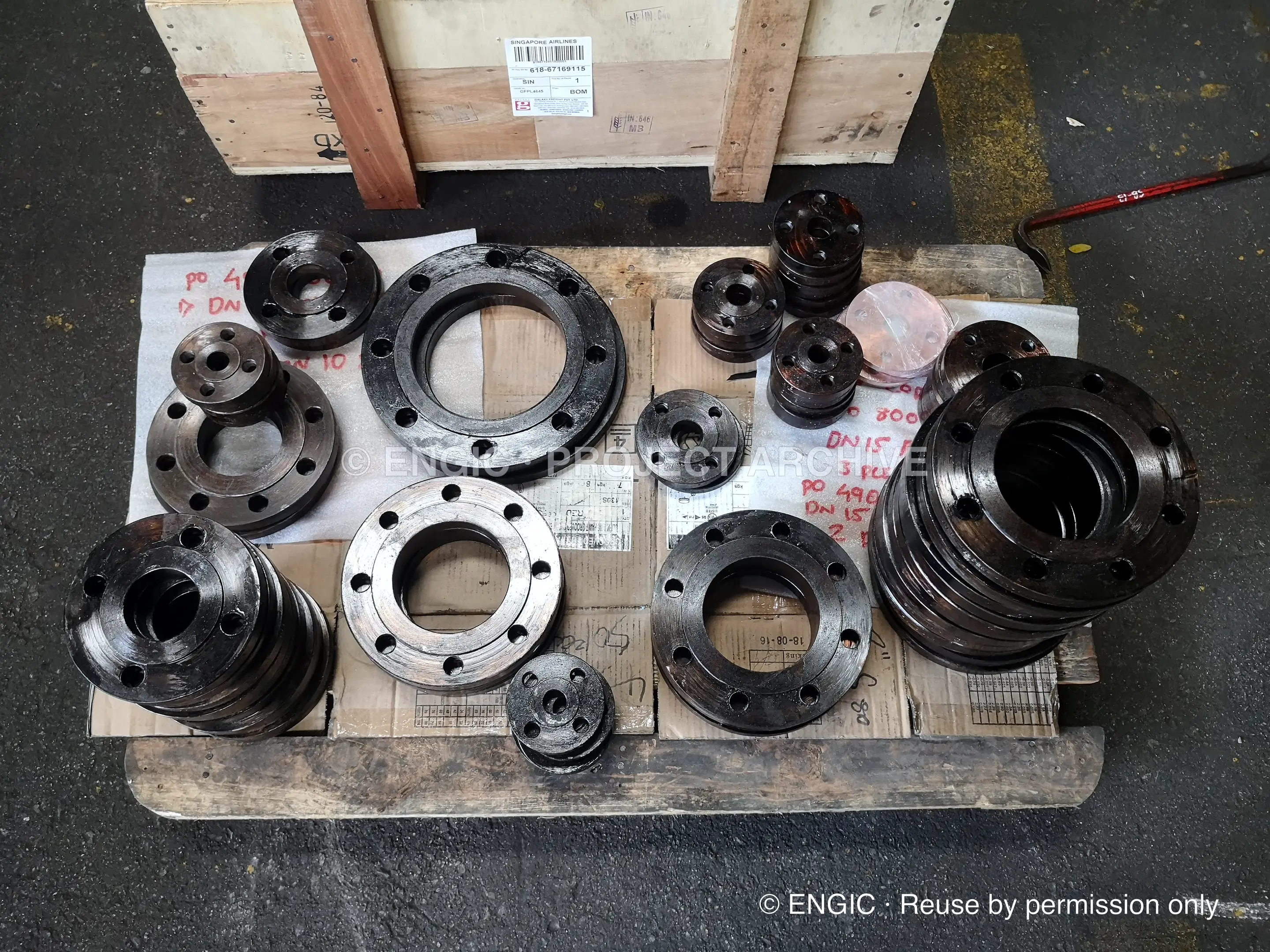 Small flanges and fittings laid out on a timber pallet with handwritten paint-pen identification marks on each piece