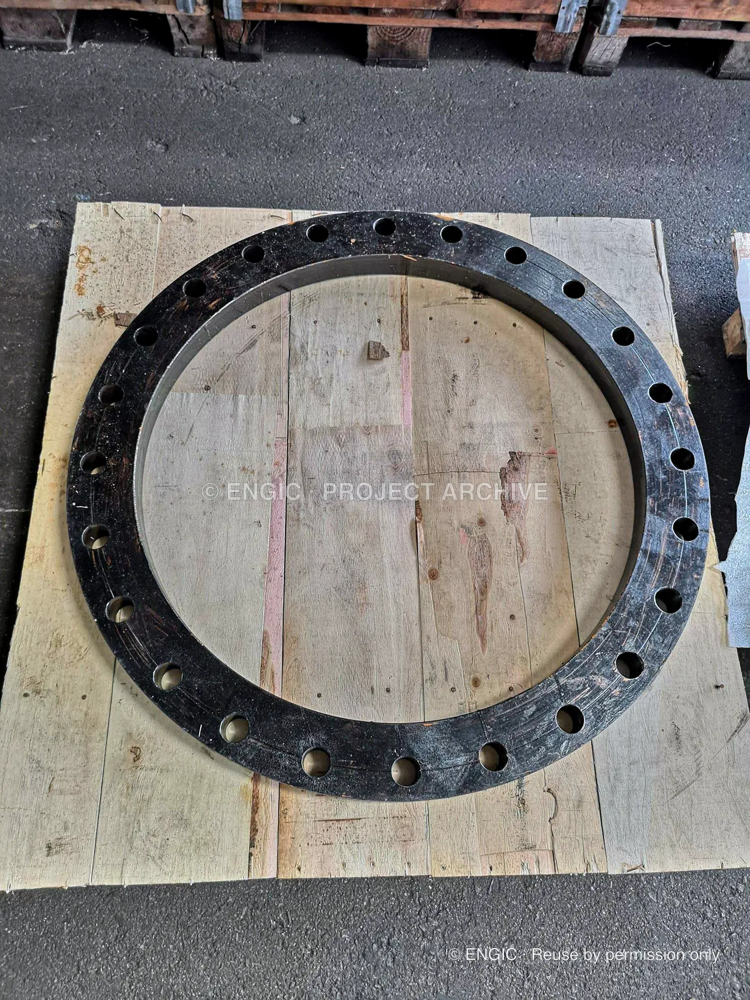 A large drilled flange ring laid flat on a timber pallet