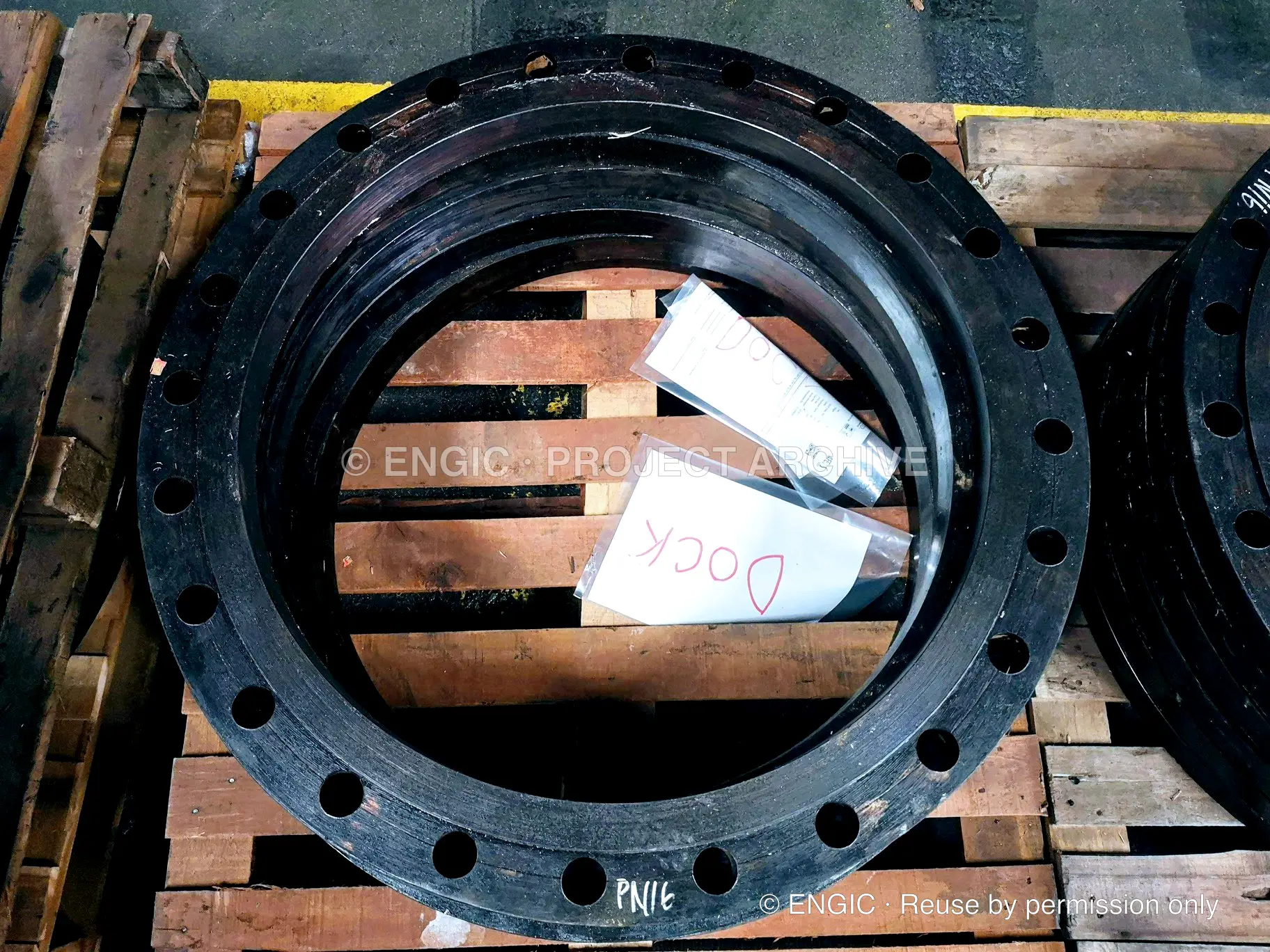 Large-bore flange rings stacked on timber pallets, hand-marked with their pressure rating and destination