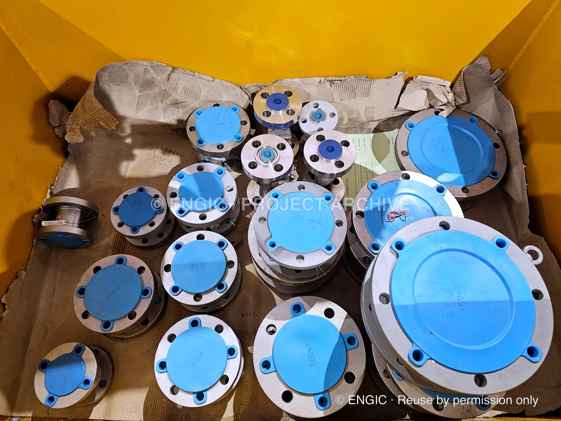 Machined flanges with blue protective covers arranged by size inside a timber crate